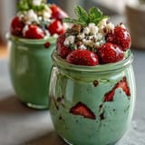 A vibrant layered jar of strawberry matcha overnight chia oats, topped with fresh berries and coconut flakes for a nourishing breakfast.