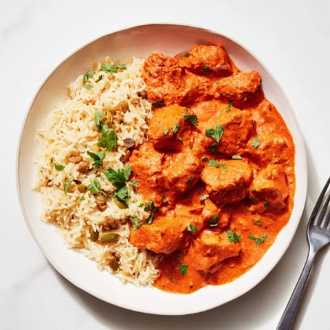 A savory plate of butter chicken, garnished with cilantro beside fluffy basmati rice.  