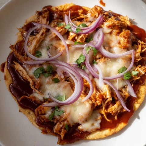 A close-up of a delicious BBQ Chicken Flatbread, loaded with shredded chicken and fragrant herbs.