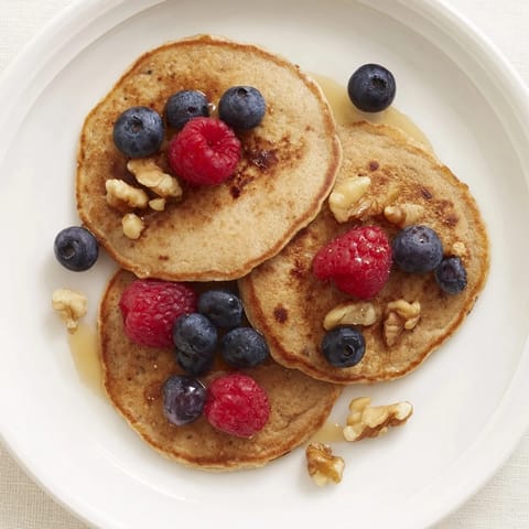 A stack of warm banana pancakes, topped with fresh berries, offer a delightful and healthy treat.