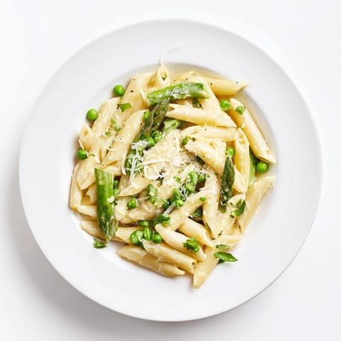 Garlic Parmesan Spring Vegetable Pasta in a white bowl, garnished with lemon zest and basil, highlighting the creamy sauce coating each piece of pasta.