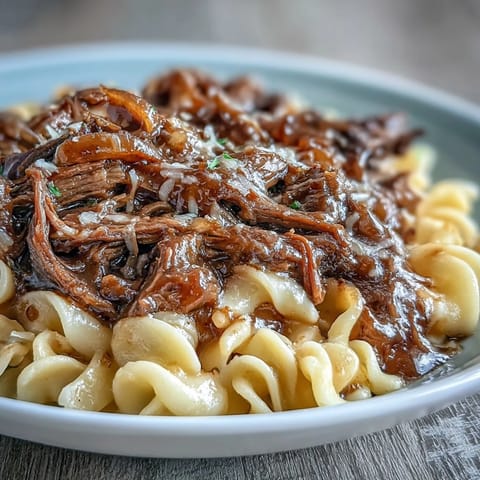 Slow-cooked pot roast with caramelized onions and tender beef served over buttery egg noodles in a savory gravy.  