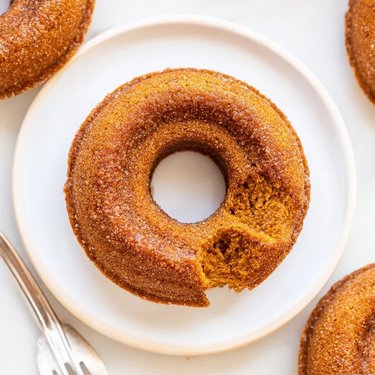 Deliciously spiced vegan pumpkin muffin donuts, baked and rolled in warm cinnamon sugar.