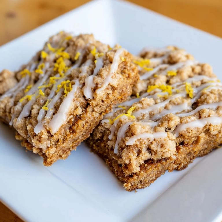 Warm, rich gingerbread crumble bars with lemon glaze, perfect for a cozy afternoon snack, invitingly delicious.