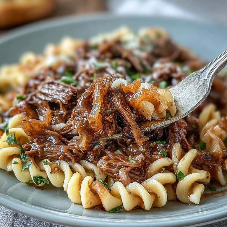 Hearty beef chuck roast simmered with wine and onions, shredded and served over wide egg noodles for a cozy meal.