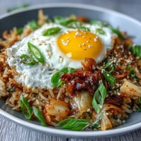 A colorful bowl of kimchi cabbage fried rice topped with a crispy fried egg and fresh green onions.